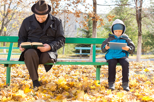 Мужчина читает книгу рядом с ребенком с планшетом