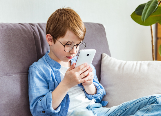 Ребенок в очках смотрит в экран смартфона